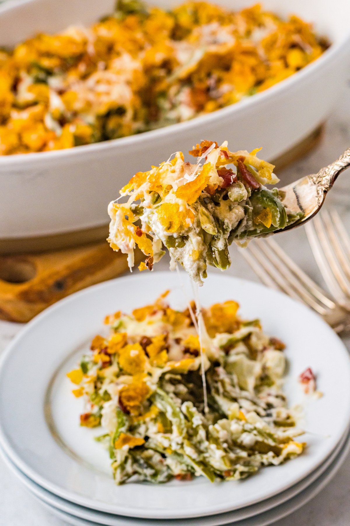A fork lifting a bite of cheesy green bean casserole toward the camera.