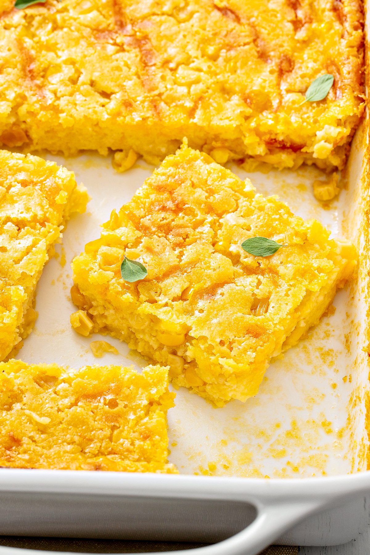With just 6 ingredients, this classic Jiffy corn casserole recipe is easy enough for a weeknight dinner, but tasty enough for a holiday meal! Sliced creamed corn casserole in a white baking dish.